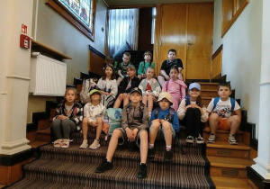 Zdjęcie przedstawia dzieci siedzące na schodach Łódzkiej Szkoły Filmowej