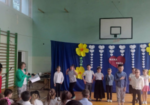 Zdjęcie przedstawia dzieci występujące na scenie podczas uroczystości